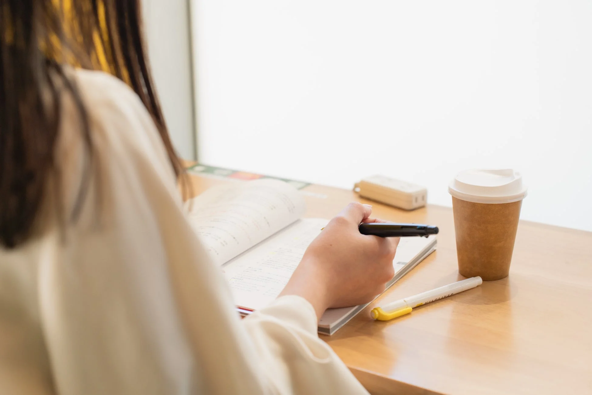 女性がカフェのような場所で勉強や仕事をしている様子。