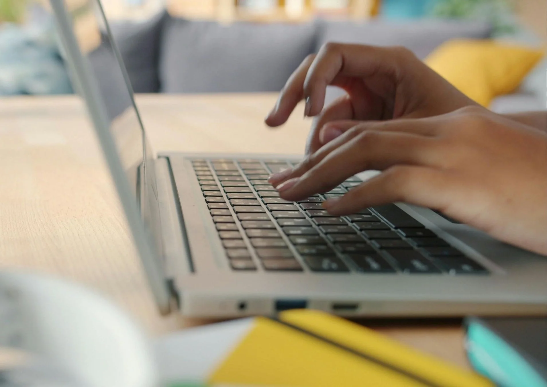 自宅またはオフィスのような環境で、人物が銀色のノートパソコンのキーボードを操作している様子