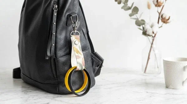 黒いレザーのリュックサックに、カラフルな柄のキーホルダーと黄色と黒のリングが取り付けられています。