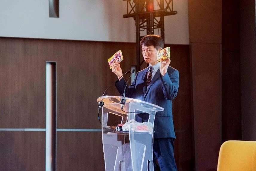 スーツを着た男性が壇上でプレゼンテーションしている