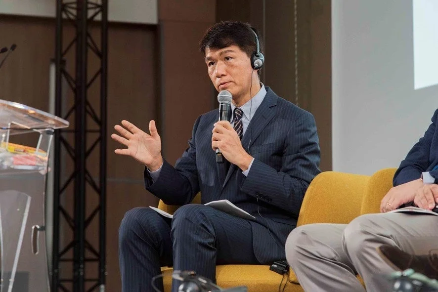 スーツを着た男性がマイクを手に話している様子