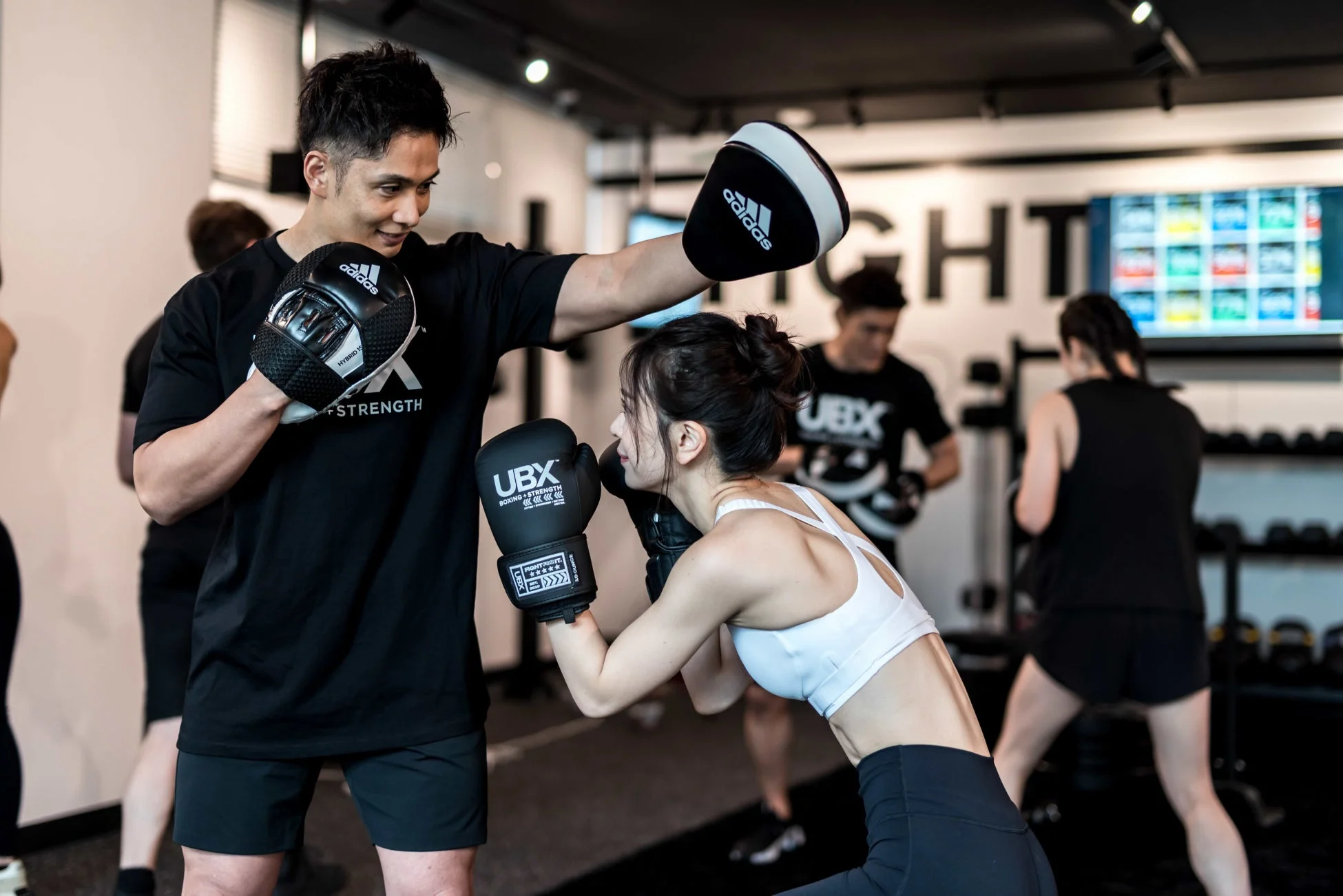 ジムで男性トレーナーがミットを持ち、女性がボクシンググローブをつけてパンチの練習をしている様子