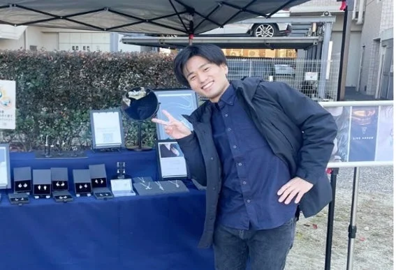 笑顔でピースサインをする男性とジュエリー販売ブース