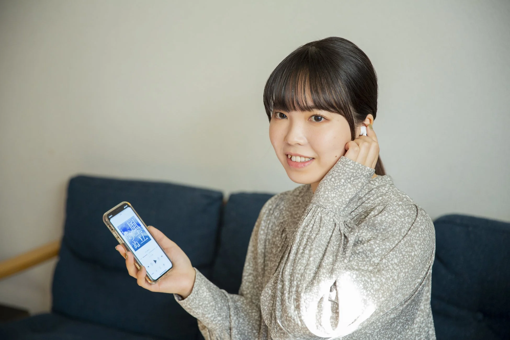 ソファでワイヤレスイヤホンを装着しスマートフォンを操作する女性