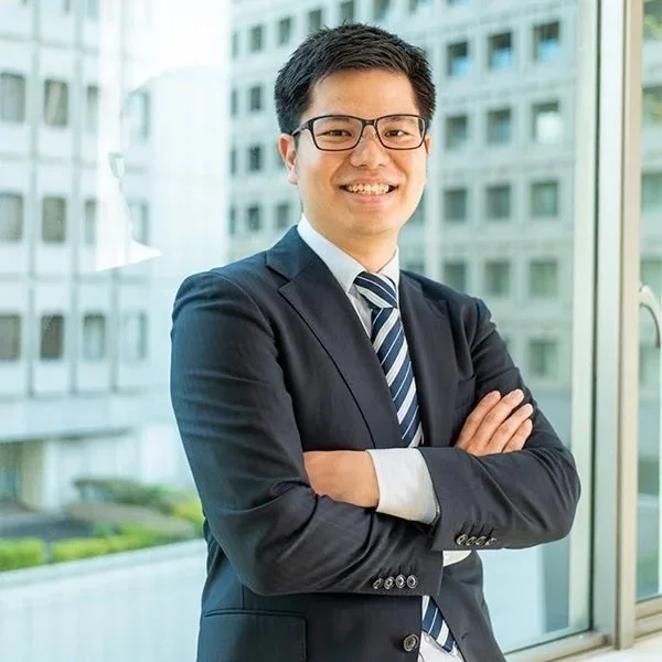 窓際で腕を組み、笑顔でこちらを見ているアジア系のビジネスマンの男性のポートレート