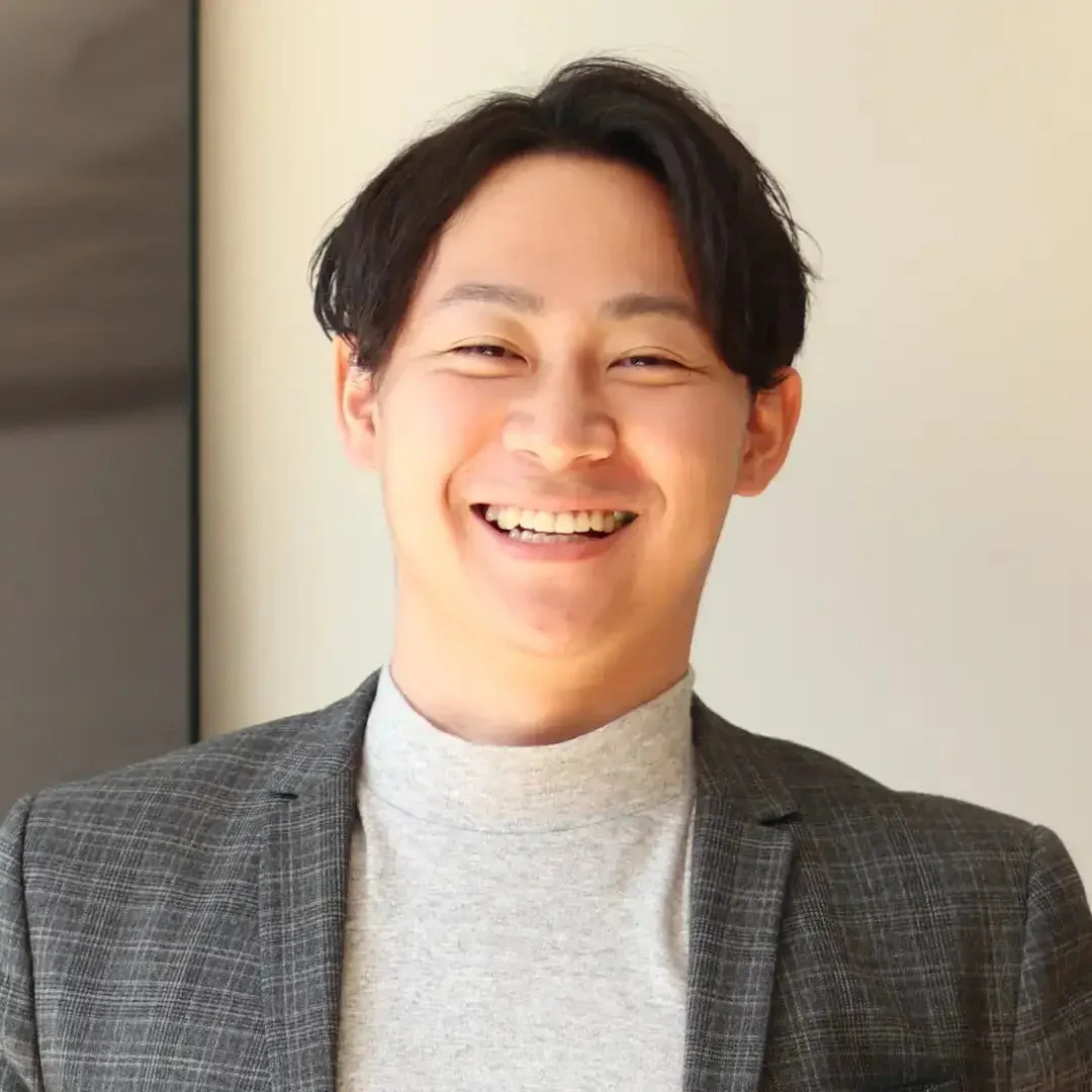 グレーのジャケットとタートルネックを着用したアジア人男性が満面の笑みを浮かべているポートレート写真