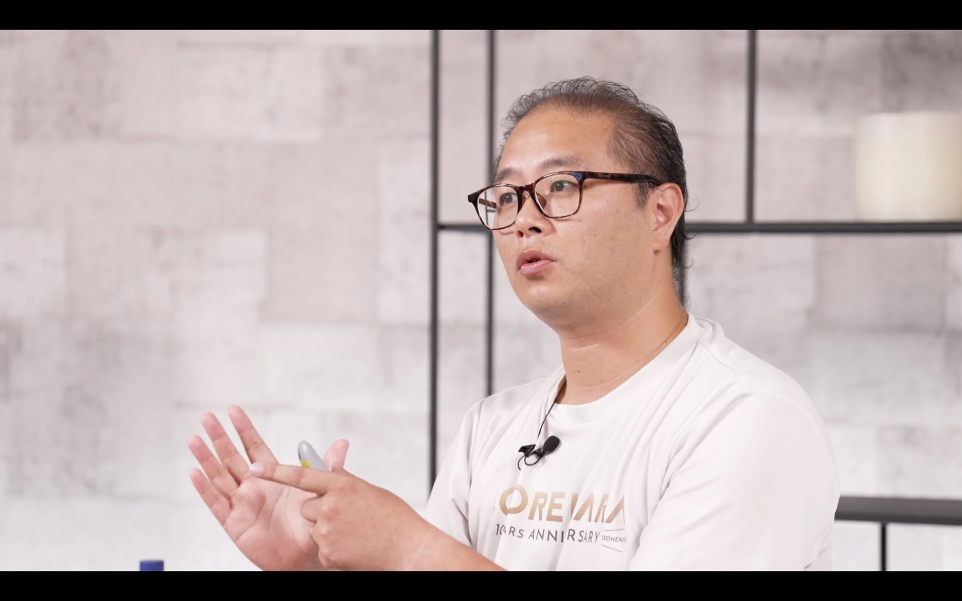 眼鏡をかけた男性が白いTシャツを着て、室内で話しています。