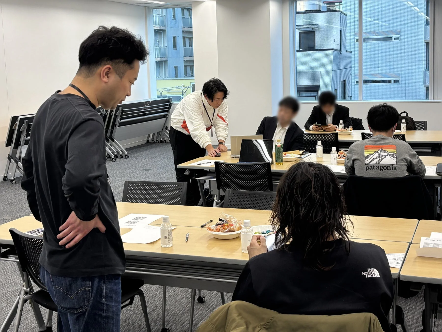 オフィスまたは会議室で数人が集まり、作業や話し合いをしている様子です。