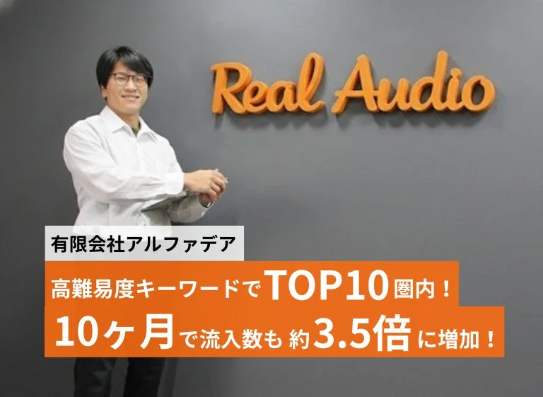 Real Audioのロゴがある壁の前で、有限会社アルファデアの成果を示す男性の画像
