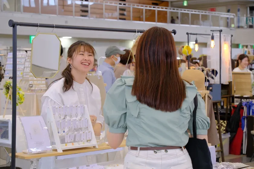 出店ブースでアクセサリーを販売し、お客さんと交流する女性