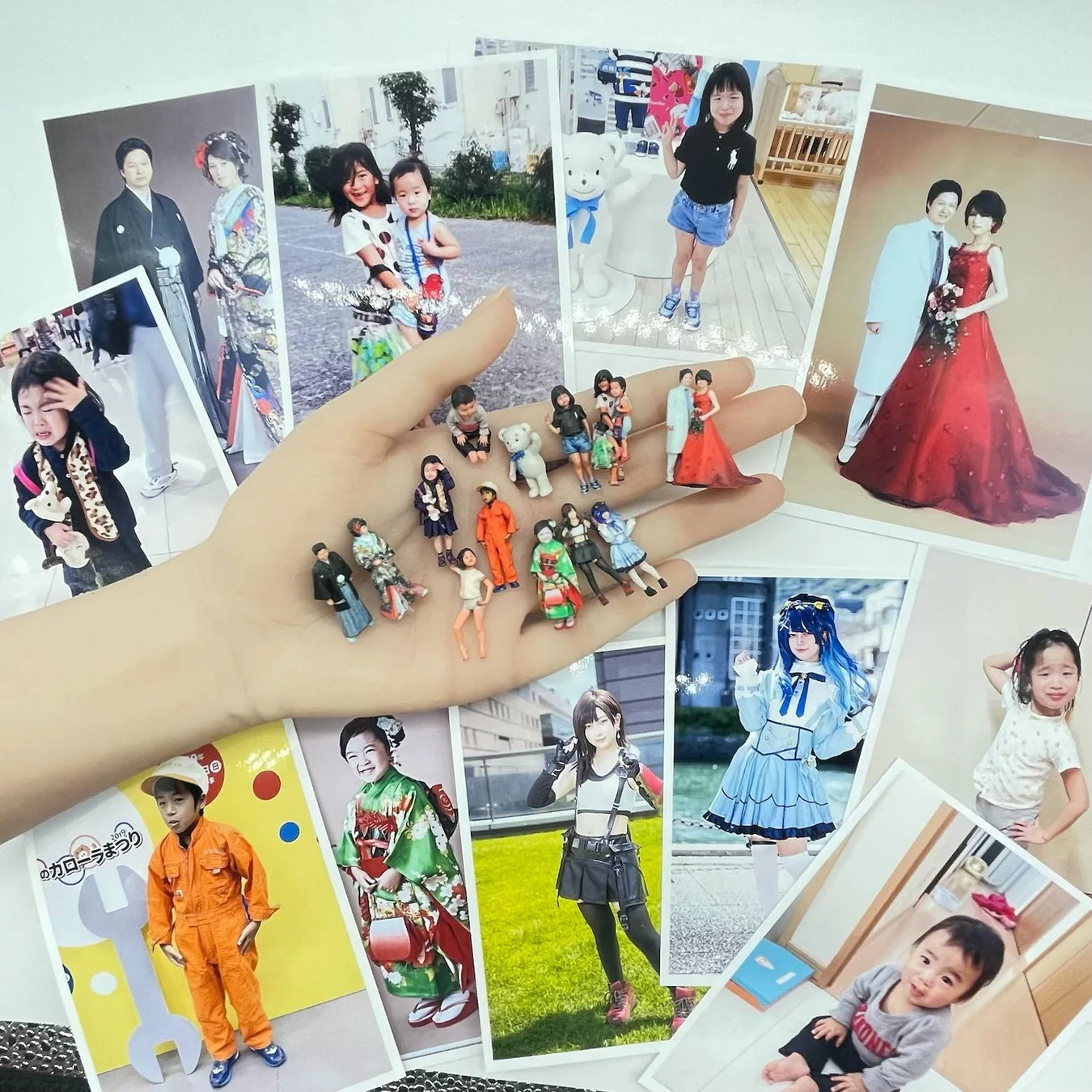 手のひらに多数のミニチュアフィギュアが乗せられており、その周りには家族の成長や特別な瞬間を捉えた様々な記念写真が散りばめられています
