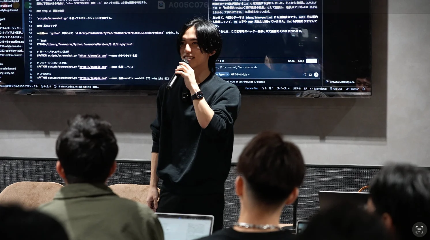 マイクを持った男性が聴衆に向けてプレゼンテーションを行っている