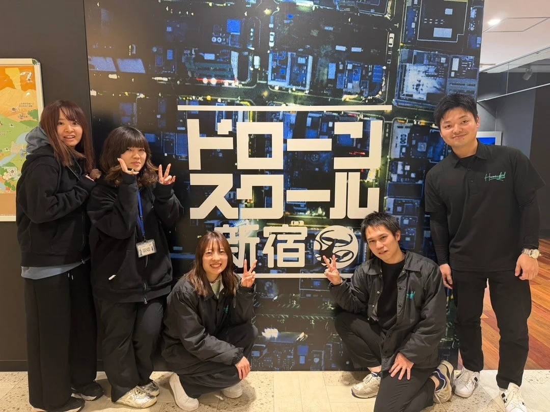 「ドローンスクール 新宿」と書かれた壁の前で、3人の女性と2人の男性が笑顔でポーズをとっている集合写真