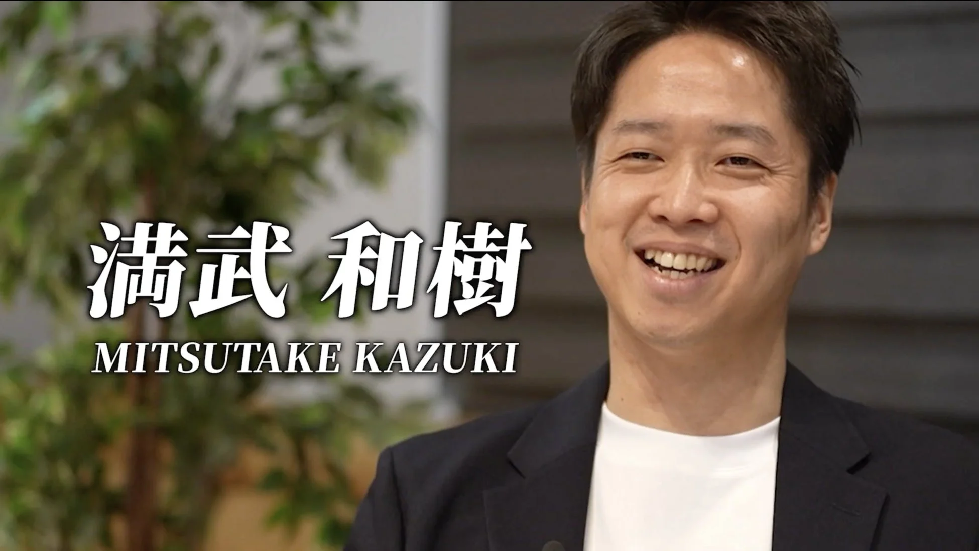 笑顔で写る男性のポートレート写真。黒いジャケットと白いTシャツを着用し、氏名「満武 和樹 (MITSUTAKE KAZUKI)」が表示されている。
