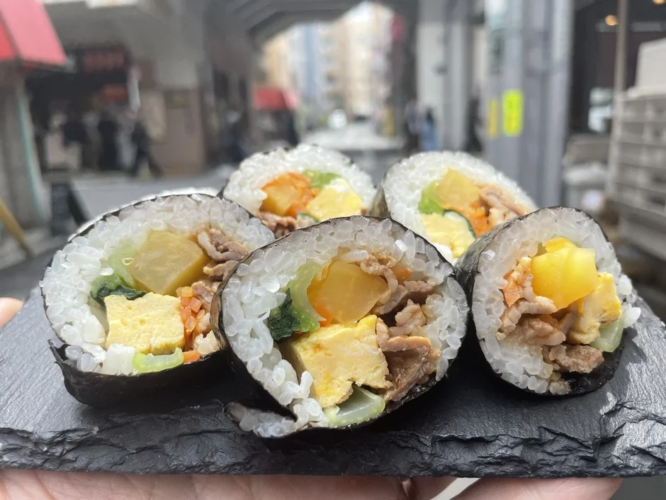 屋外で撮影された、スレート調の皿に盛り付けられたキンパのクローズアップ写真です。