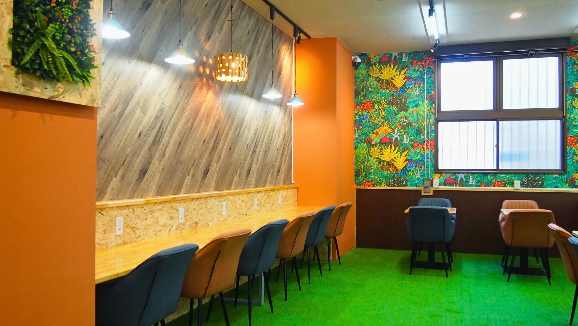 カラフルなトロピカル柄の壁紙と鮮やかな人工芝の床が特徴的な、モダンでおしゃれなカフェまたはコワーキングスペースの内観
