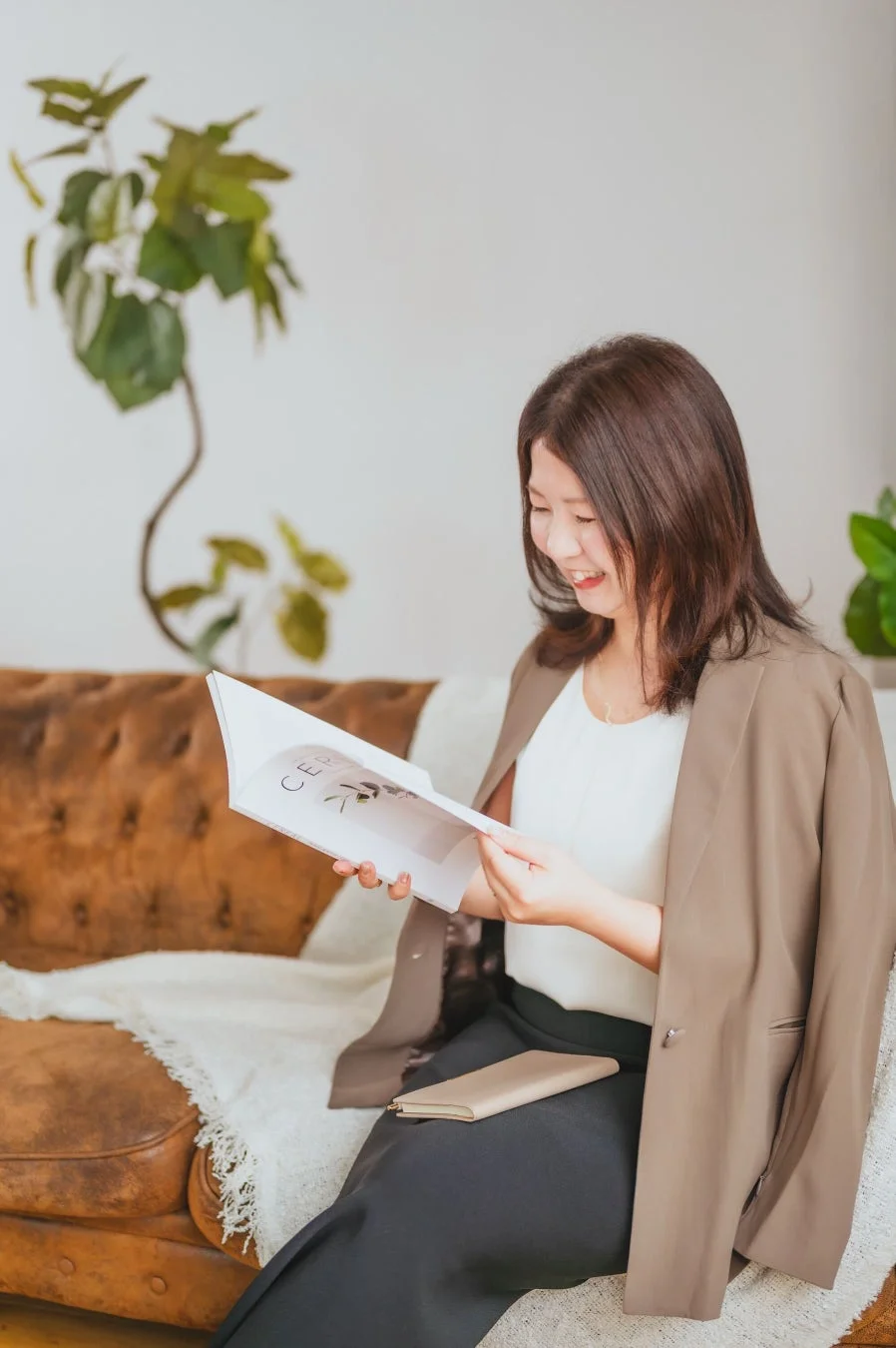 笑顔の女性が茶色のソファに座り、雑誌を読んでいます
