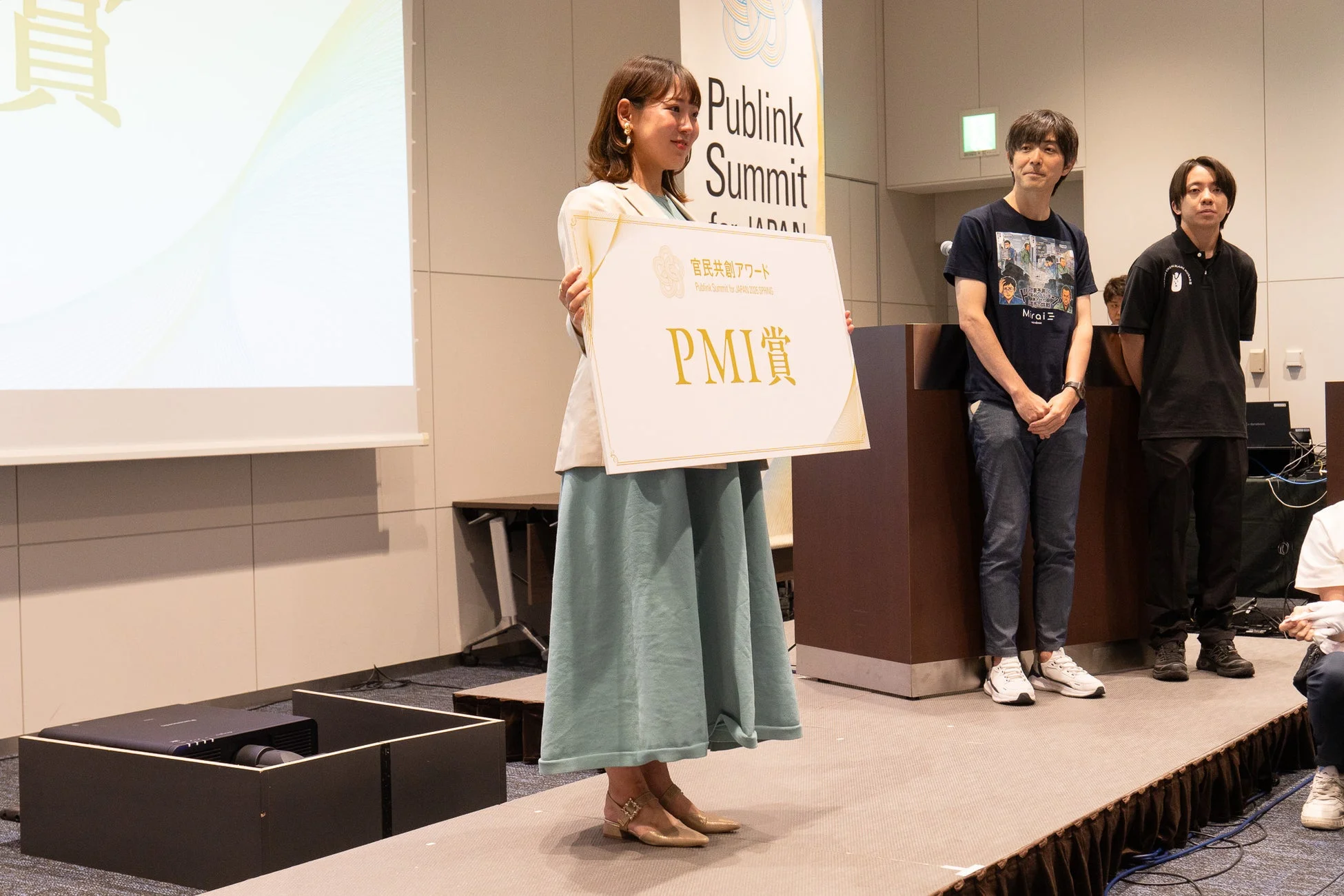 Publink Summitのイベント会場で「PMI賞」と書かれた賞状を掲げる松尾真里氏