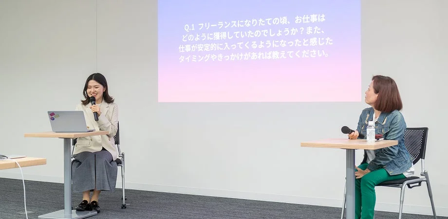フリーランスの仕事獲得や安定化に関する質問がスクリーンに投影された会場で、2人の女性がセミナーやパネルディスカッションに参加している様子