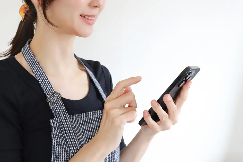 エプロンを着用した女性がスマートフォンを操作