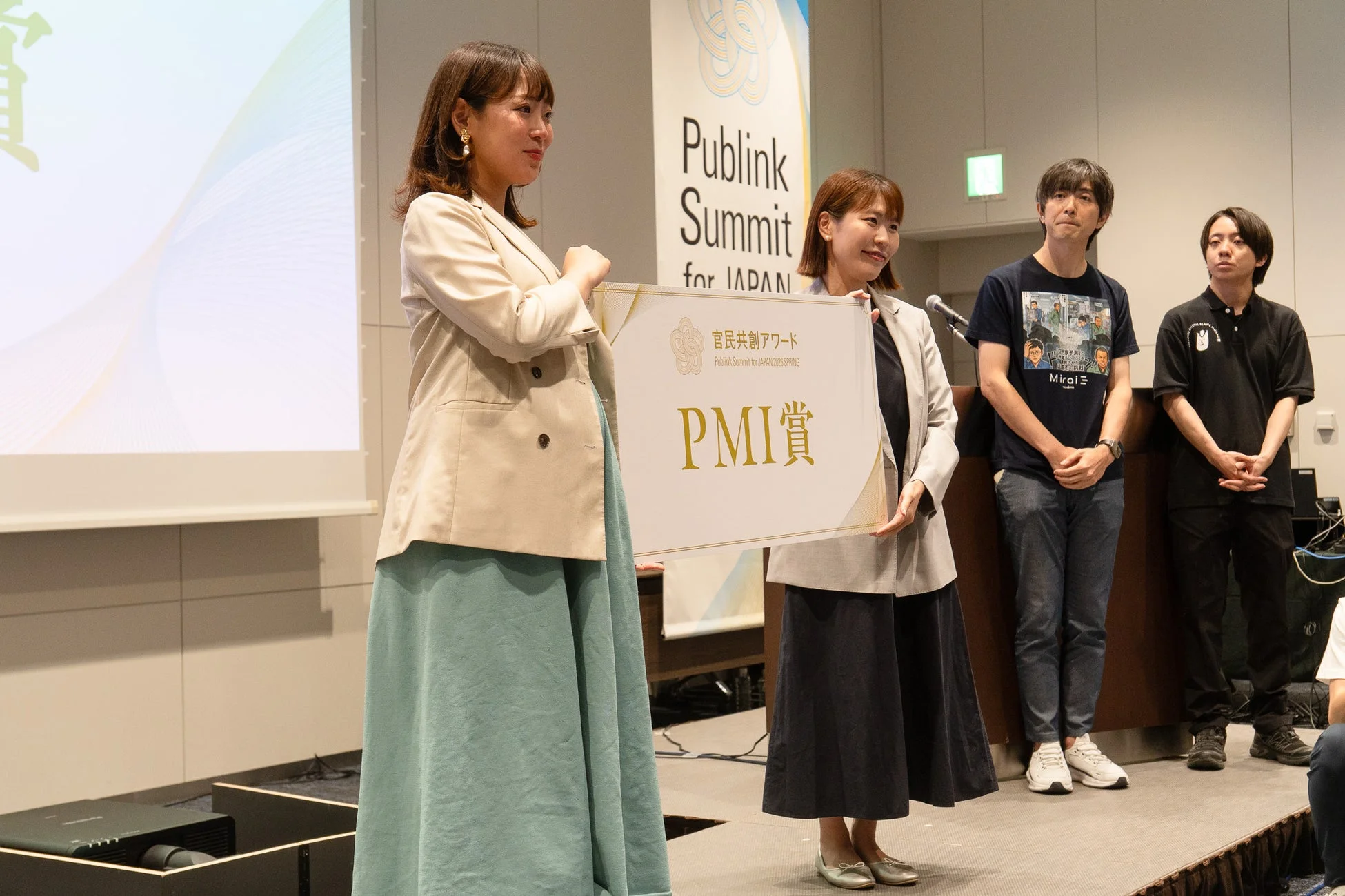 ステージ上で「PMI賞」の賞状を掲げる松尾真里氏と関係者