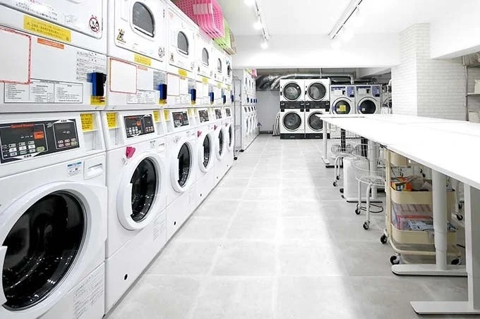 多数の白を基調とした洗濯機と乾燥機が並ぶ、清潔感のあるモダンなコインランドリーの内部