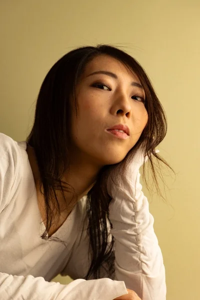 薄緑色の背景を背に、白い長袖シャツを着た若いアジア人女性のポートレート