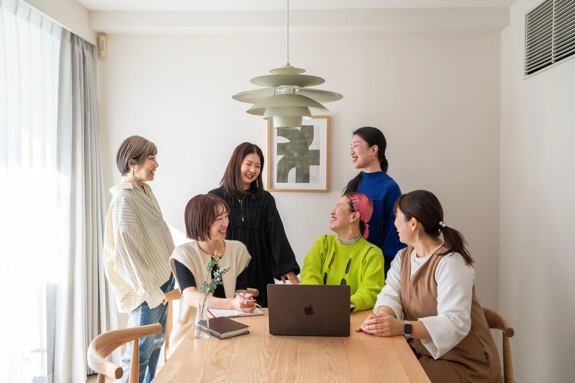 6人の女性がテーブルを囲み、ノートパソコンを見ながら笑顔で会話している様子