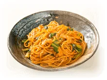 素焼きのような質感の器に盛り付けられた、オレンジ色のソースで和えられたスパゲッティ
