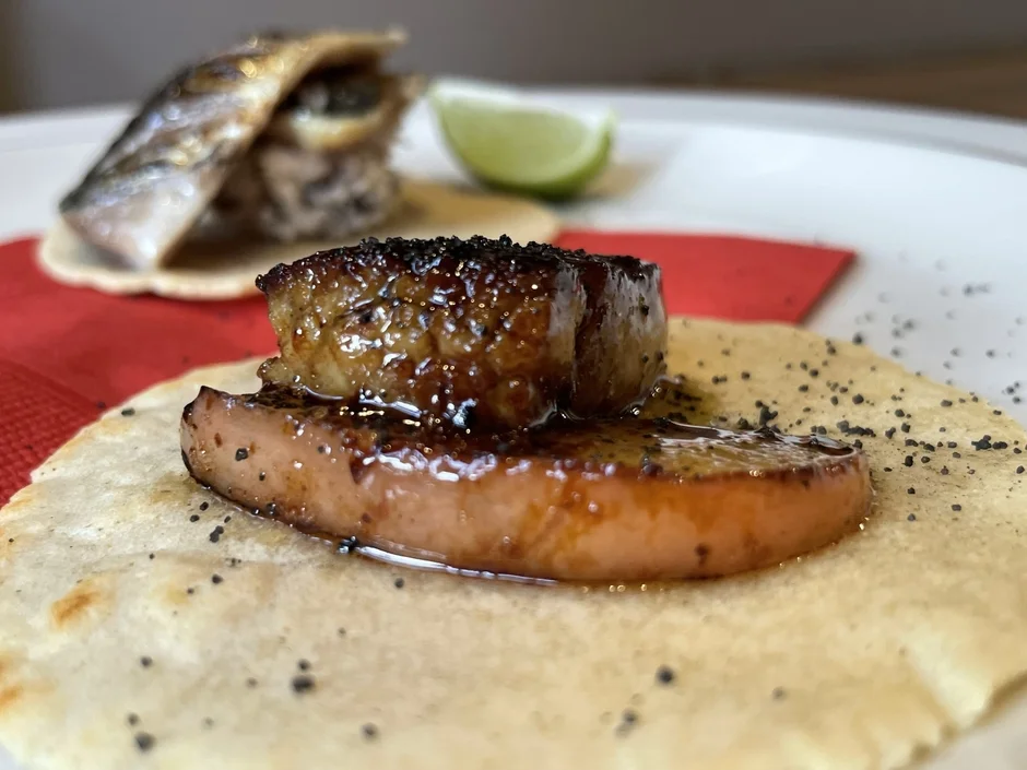 手前にはフォアグラと果物のソテーがトルティーヤに乗った料理、奥には魚のグリルが乗った料理が見えます。ライムが添えられたおしゃれな創作料理です。