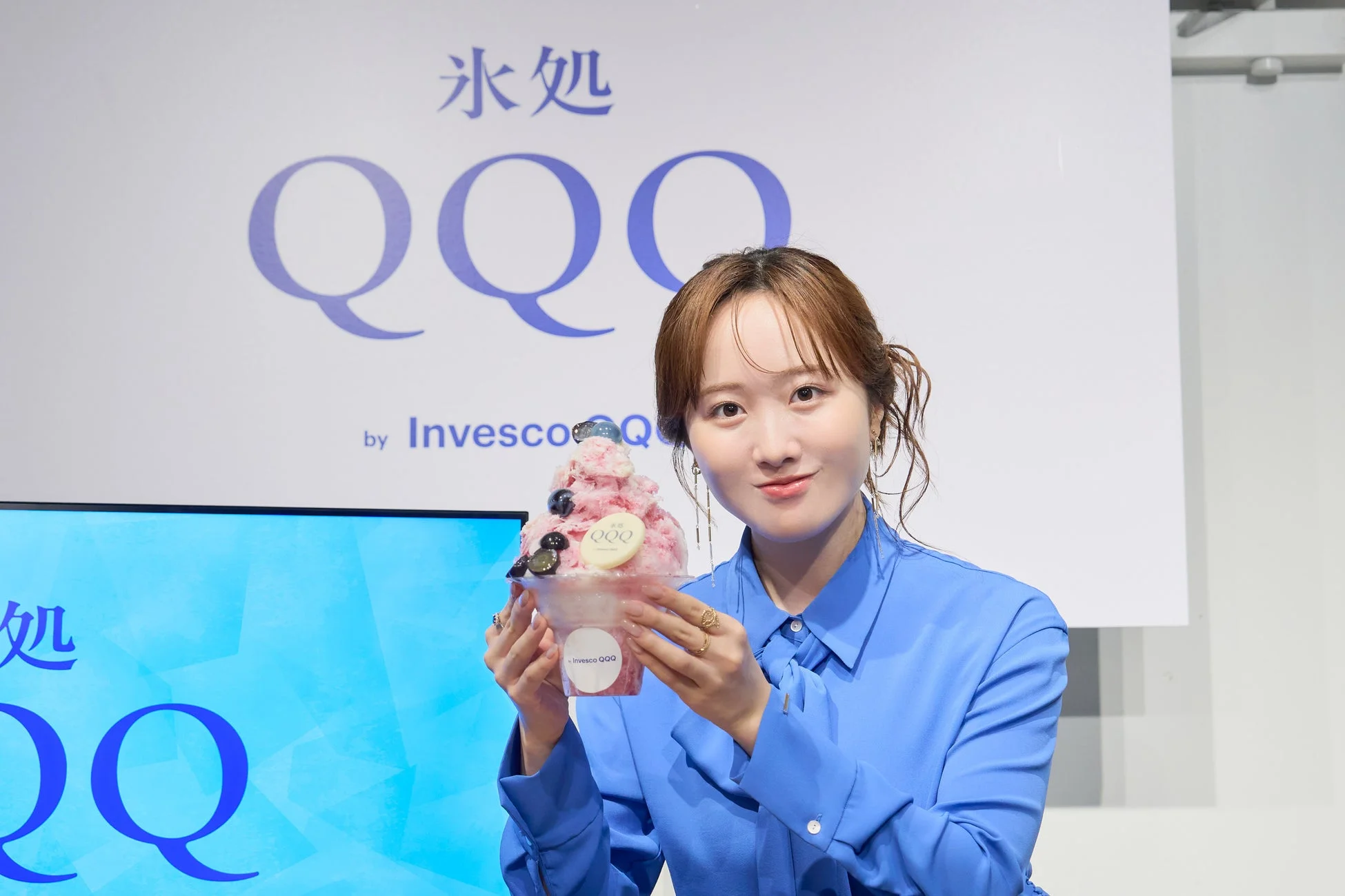青いシャツを着た女性がピンクのかき氷を笑顔で手にしている